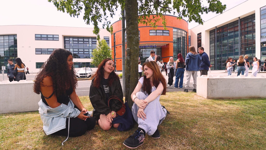 three female students are sitting and talking by a tree