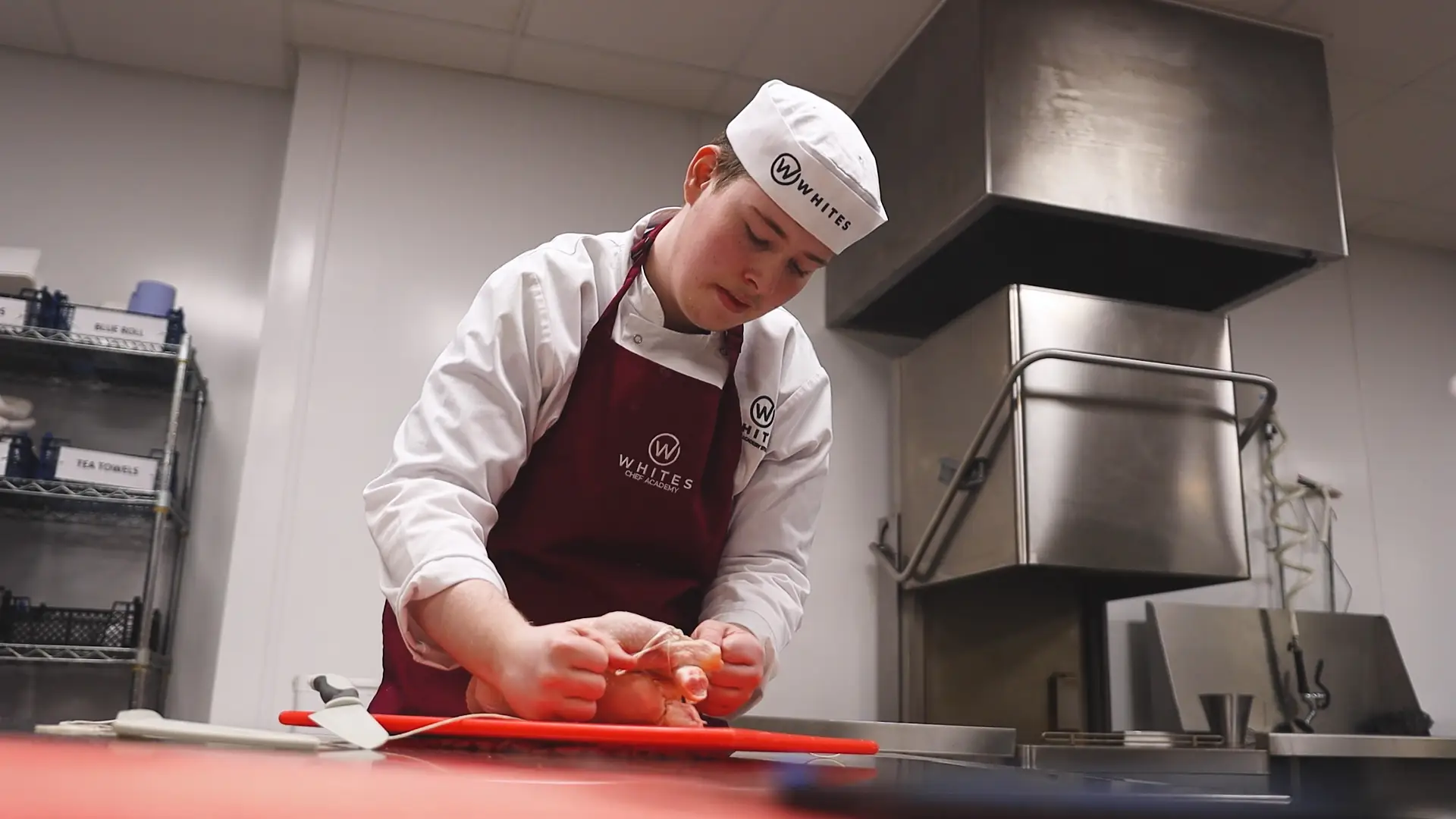 a whites chef academy student is putting string around chicken meat on a chopping board