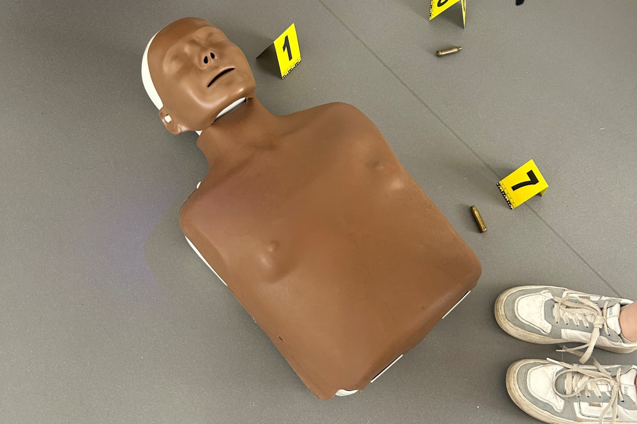 A CPR dummy and yellow numbers have been placed on the floor as part of a crime scene activity.