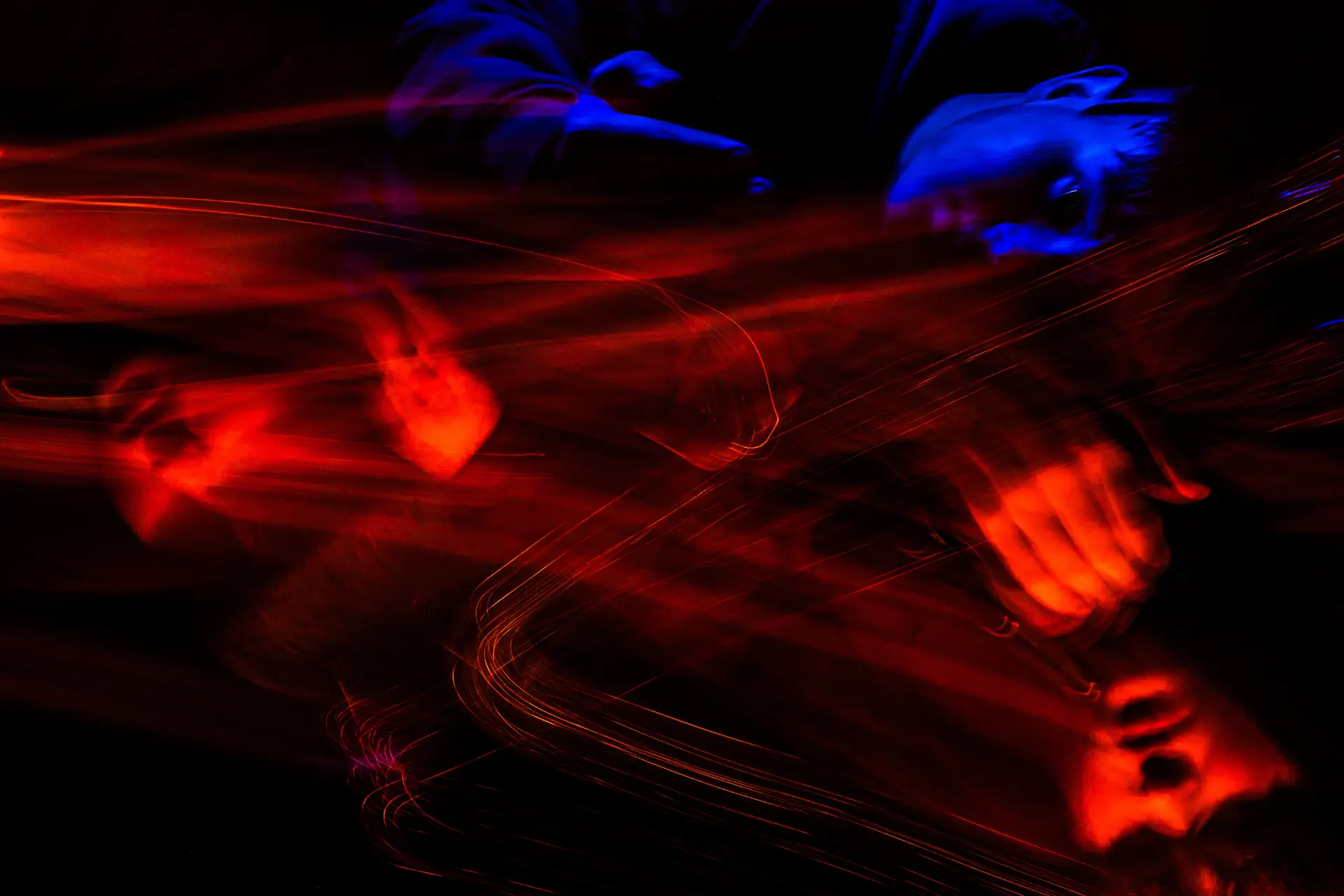 Abstract long exposure photograph of a person lying on their side, illuminated with blue light and intersected by flowing red light trails against a black background.