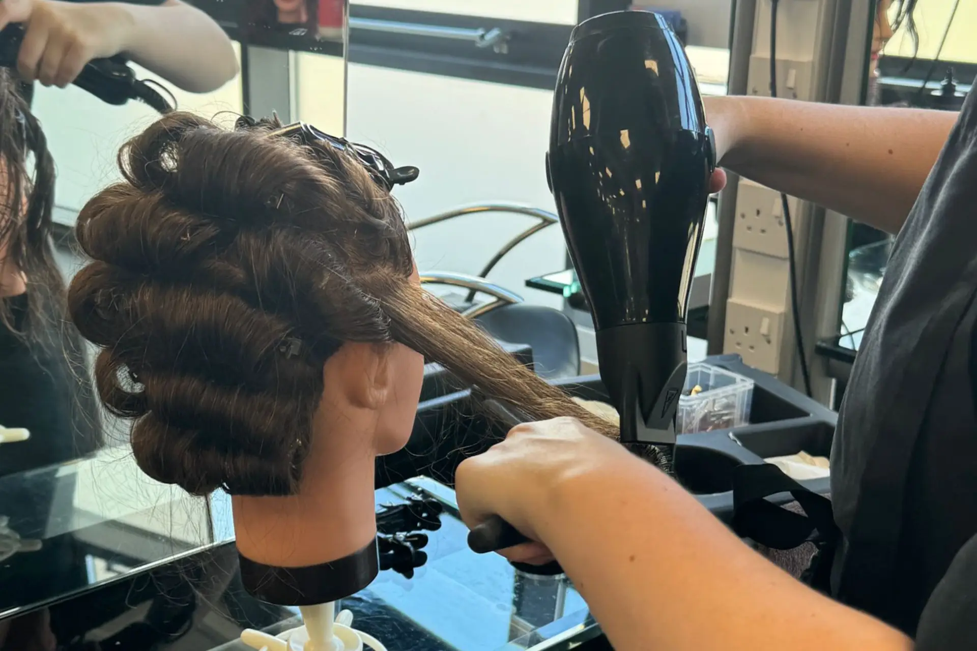 A hairdressing student is practising blow-drying techniques on a mannequin head