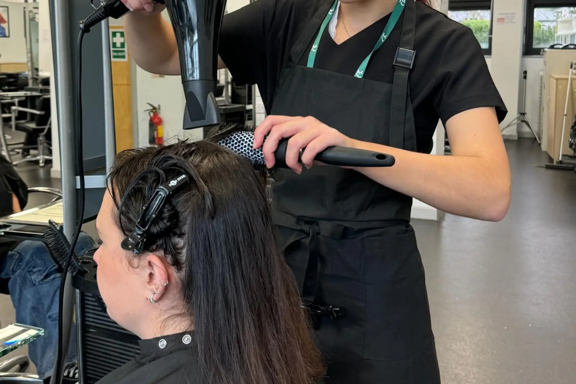 A hairdressing student is blow-drying a client's hair.