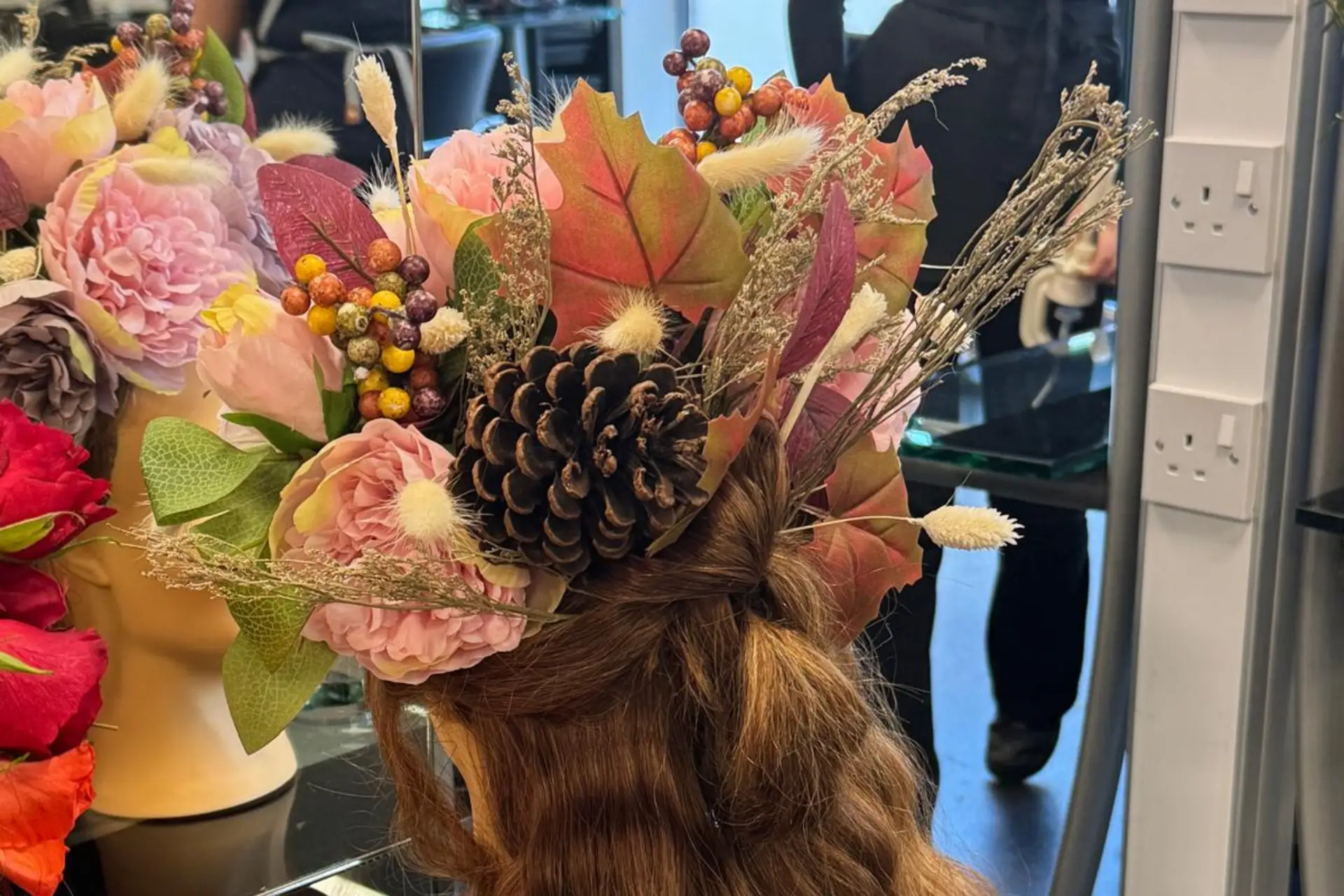 A mannequin head has been decorated with an autumn themed hairstyle featuring brightly coloured leaves, berries, flowers, and a pinecone.