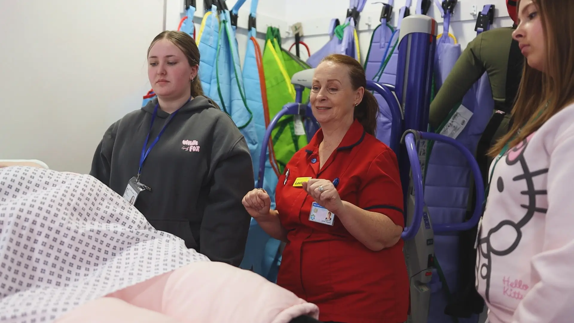 Two female health students and a hospital worker are looking at a hospital bed.