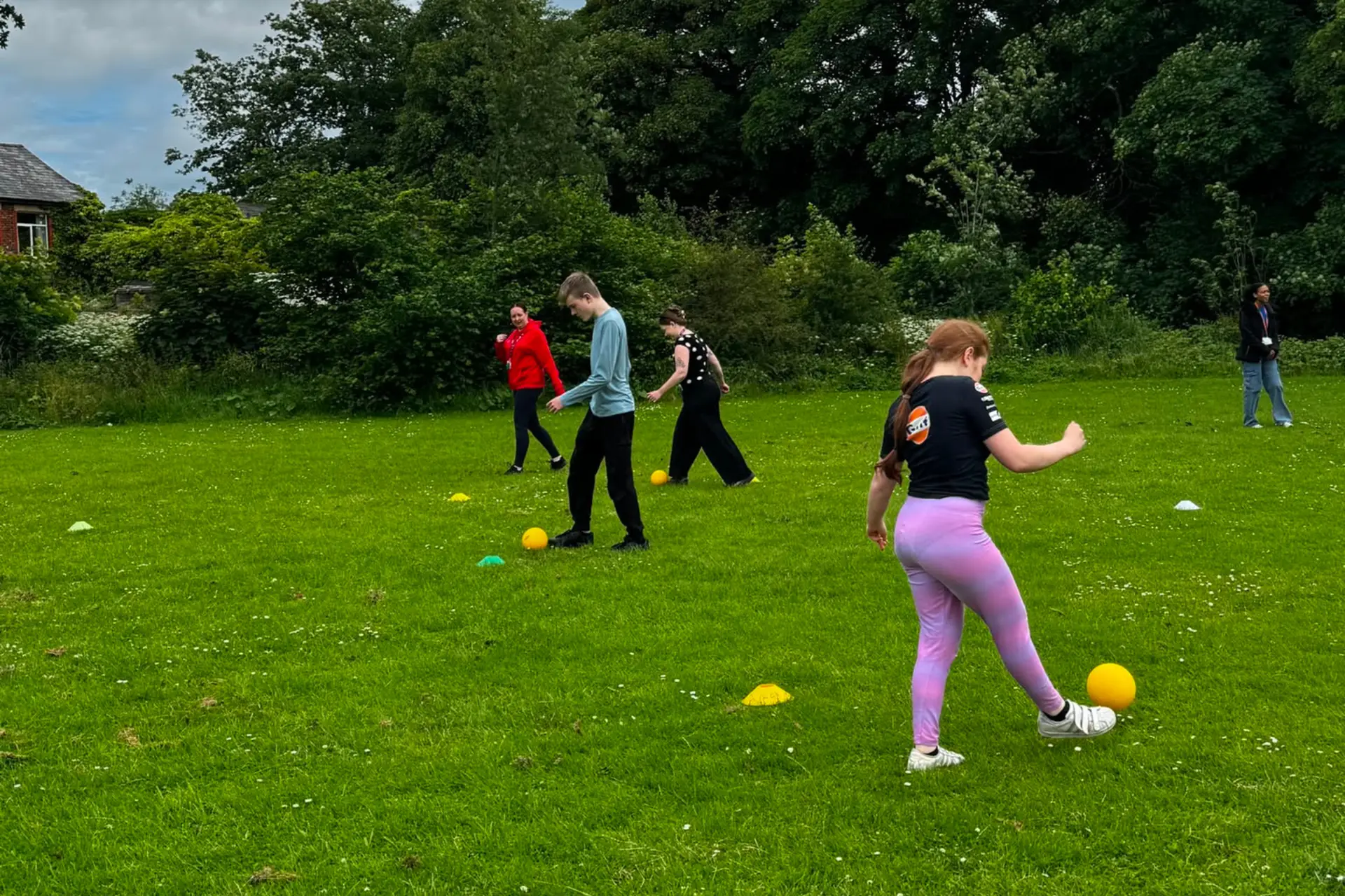 A group of pathways students are taking part in a sports day event. They are kicking footballs.