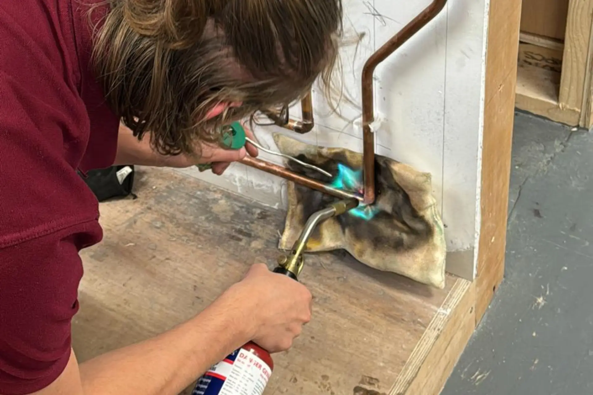 A plumbing student is using a blow torch to solder pipework together