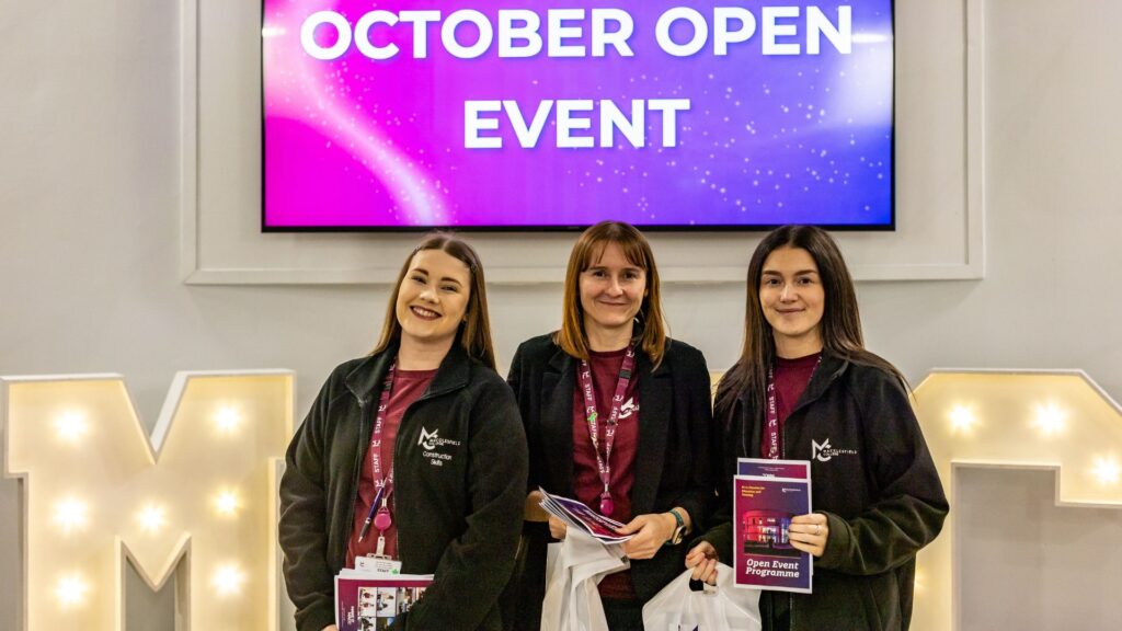 Three female staff members stand in front of light up letters