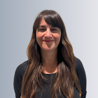 A headshot of a female staff smiling, behind them is a grey background