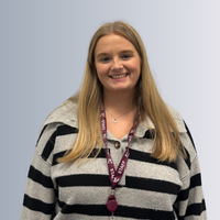 A headshot of a female staff smiling, behind them is a grey background