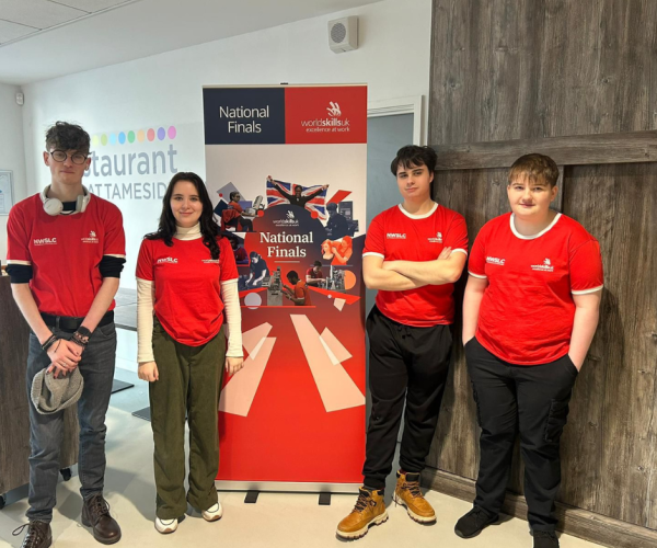 Four Creative Media students are smiling for a photo while they stand next to a National Finals World Skills UK banner.