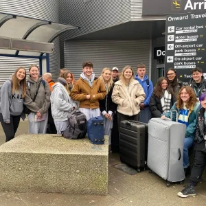 A group of students are standing in front of an airport and smiling for a photo