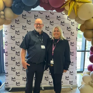 Two people standing under a balloon arch, smiling for a photo