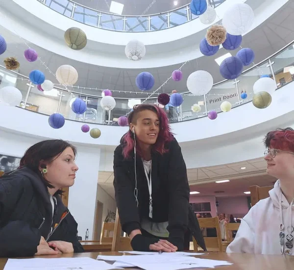 A group of students talking happily in macclesfield college foyer with the ceiling filled with balloons