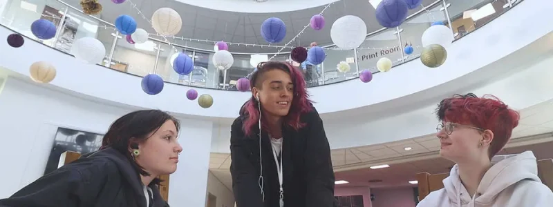 A group of students talking happily in macclesfield college foyer with the ceiling filled with balloons